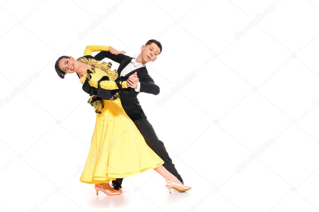 smiling elegant young couple of ballroom dancers in yellow dress and black suit dancing on white