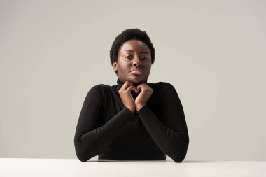 Siyah balıkçı yaka yakalı güzel Afro-Amerikalı kadın gri masada tek başına oturuyor.