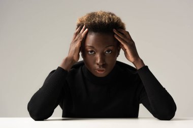 Siyahi balıkçı yaka kazaklı çekici Afro-Amerikan kadın gri masada tek başına oturuyor.