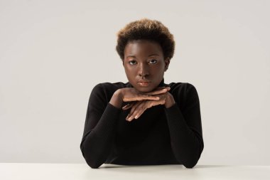 Siyahi balıkçı yaka kazaklı Afro-Amerikan kadın gri masada tek başına oturuyor.