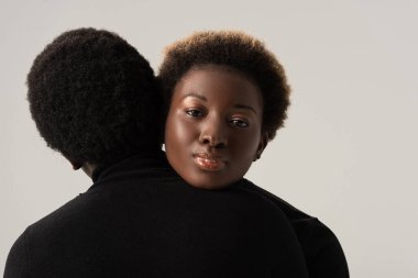Siyah balıkçı yaka kazaklı Afro-Amerikan kızları Gri üzerine izole edilmiş bir şekilde sarılıyorlar