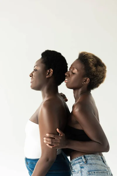 smiling african american women in tops hugging isolated on grey