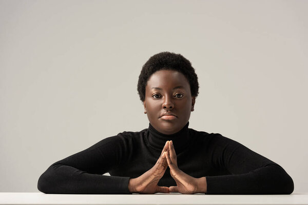 thoughtful african american woman in black turtleneck sitting at table isolated on grey