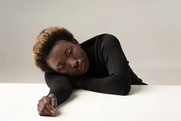 Втомлена Афроамериканська Жінка Чорному Черепасі Сидить Лежачи Столі Ізольовано Сірому — стокове фото