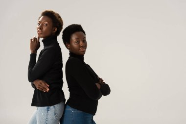 Siyahi balıkçı yaka kazaklı Afro-Amerikan kızları gri renkte sırt sırta dururlar.