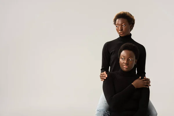 african american friends in black turtlenecks hugging isolated on grey