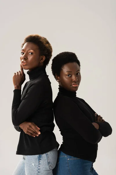 confident african american friends in black turtlenecks standing back to back isolated on grey