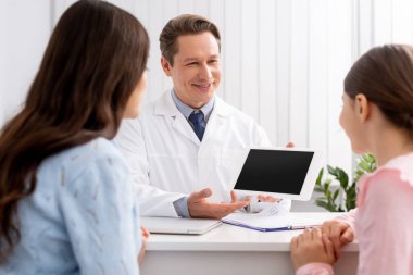 Anne ve kızın gülümseyerek dijital tableti boş ekranla gösteren doktorlara baktığı arka plan