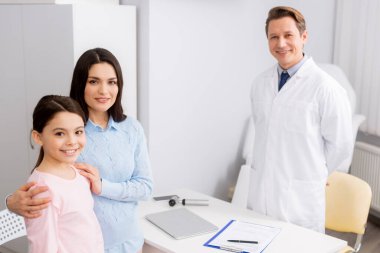 Gülümseyen doktor ve mutlu anne. Kızı kameraya bakarken gülümsüyor.