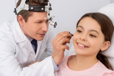 Kulak spekulumu olan sevimli bir çocuğun kulağını inceleyen özenli bir doktor.