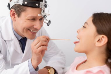 Neşeli doktor dil bastırıcılı şirin çocuğun boğazını inceliyor.