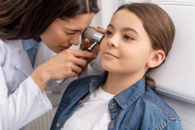 attentive otolaryngologist examining ear of adorable smiling child with otoscope clipart