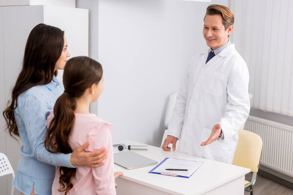 smiling ent physician looking and welcoming mother and daughter 