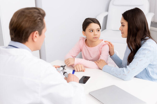smiling mother touching daughters shoulder during consultation with ent physician