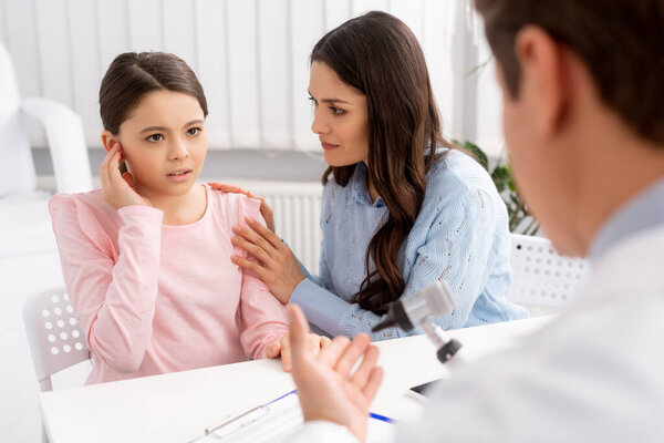 cropped view of ent physician, and woman calming daughter touching ear