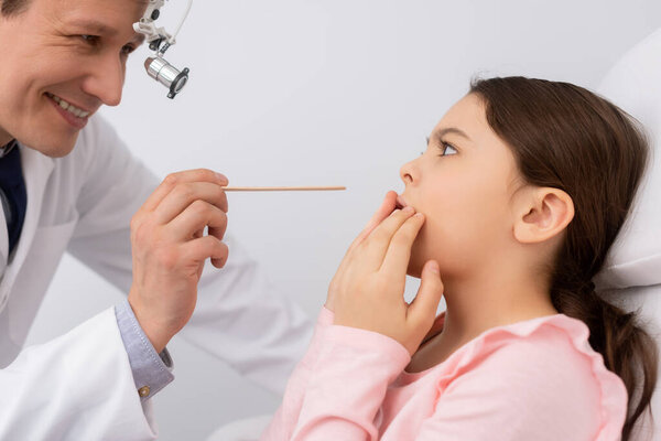 smiling ent physician holding tongue depressor near frightened child