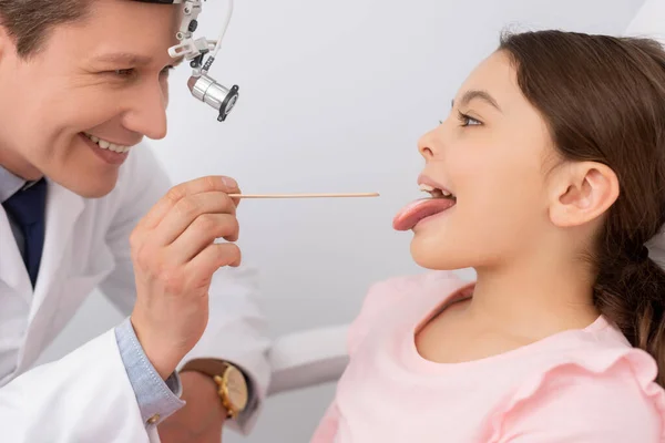 笑医生用舌头抑制剂检查可爱儿童的咽喉 — 图库照片