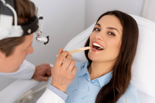 attractive woman looking at camera while ent physician holding tongue depressor 
