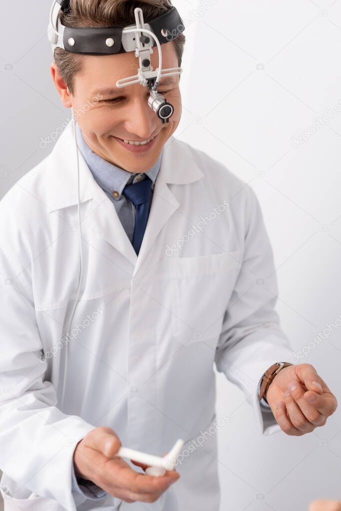 smiling otolaryngologist with ent headlight holding nasal speculum