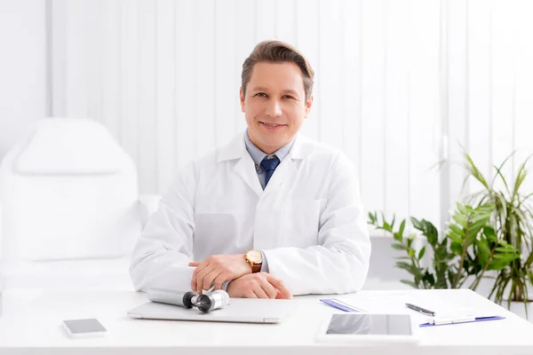 Sonriente Ent Médico Sonriendo Mientras Está Sentado Lugar Trabajo Cerca — Foto de Stock
