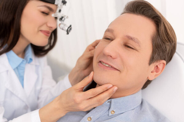 selective focus of attractive otolaryngologist in ent headlight examining ear of smiling man 