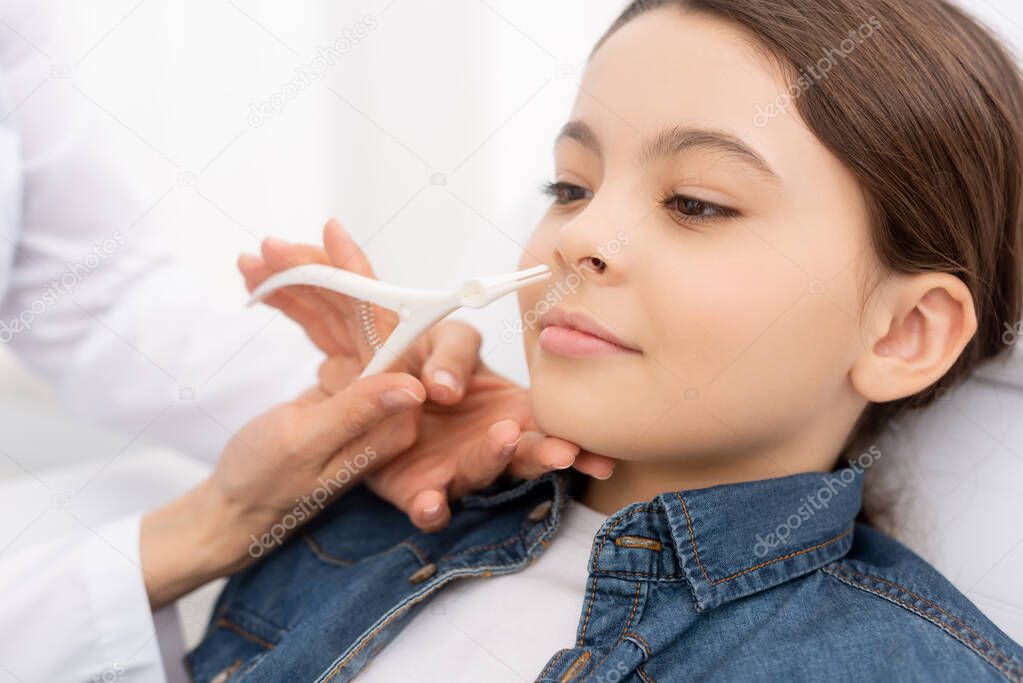 partial view of ent physician examining nose of kid with nasal speculum