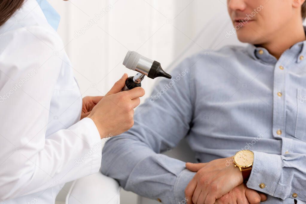cropped view of ent physician holding otoscope near patient
