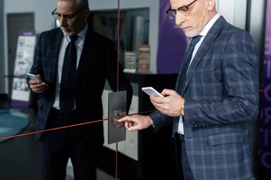 Akıllı telefon kullanan ve asansör düğmesine basan işadamının kırpılmış görüntüsü 