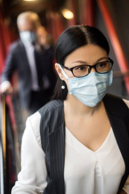 Resmi giysili Asyalı iş kadını tıbbi maskesiyle başka yere bakıyor. 
