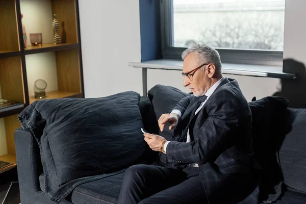 スーツ姿のビジネスマンがソファに座りホテルでスマートフォンを使う姿を — ストック写真