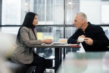 side view of businessman and asian businesswoman talking in cafe 