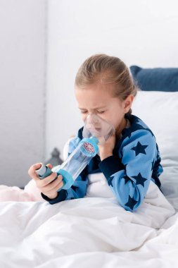 asthmatic child with closed eyes using inhaler with spacer clipart