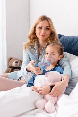 attractive mother sitting near sick daughter using inhaler with spacer  clipart
