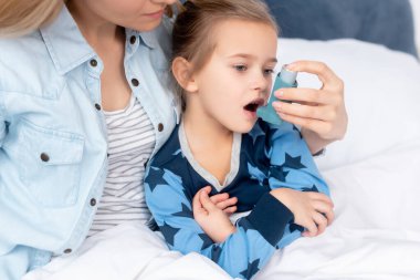 caring mother holding inhaler with spacer near sick daughter  clipart