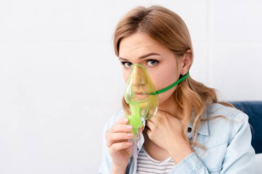 asthmatic woman holding respiratory mask near face and looking at camera clipart