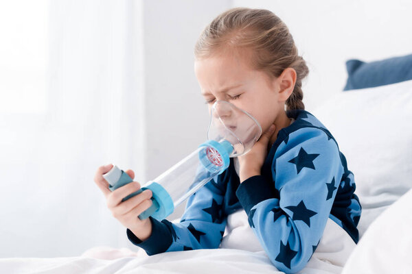 sick child with closed eyes using inhaler with spacer