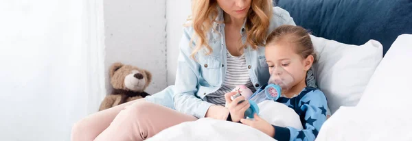 Tiro Panorámico Madre Cariñosa Sentada Cerca Hija Enferma Usando Inhalador —  Fotos de Stock