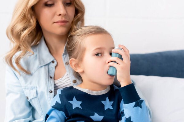 caring mother looking at sick daughter using inhaler
