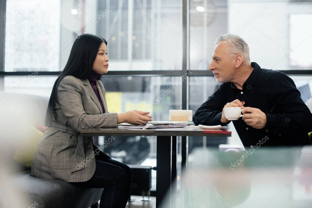 side view of businessman and asian businesswoman talking in cafe 