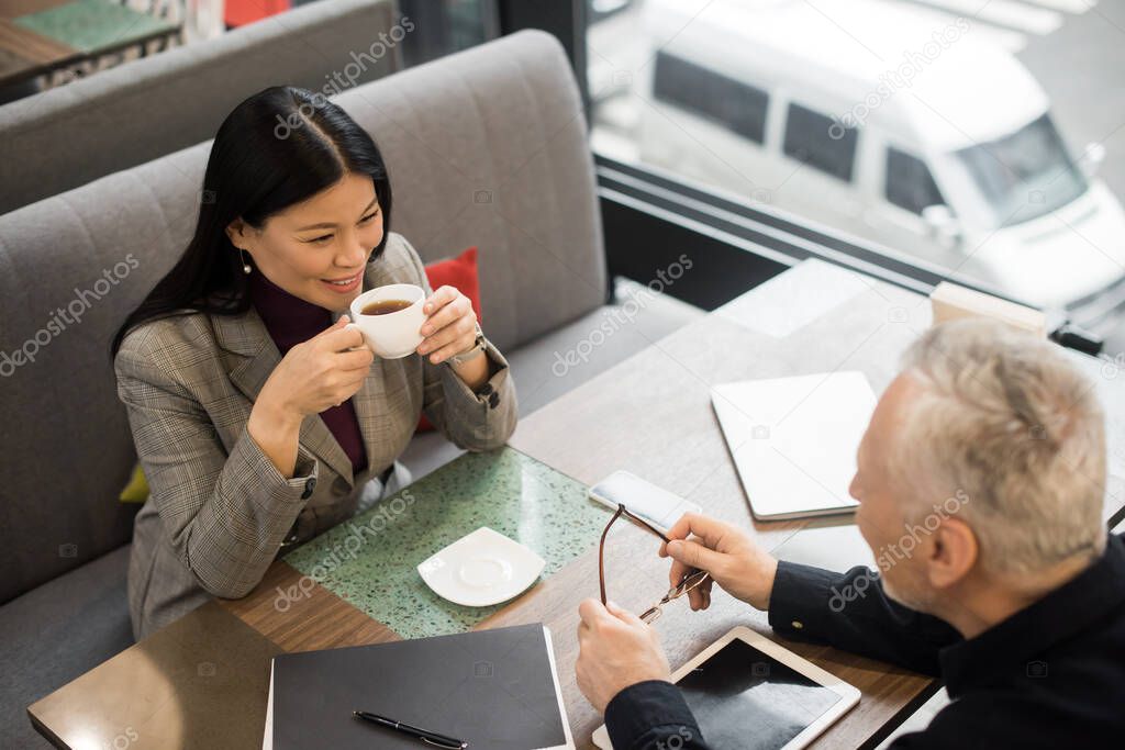 high angle view of businessman and asian businesswoman with cup talking in cafe 