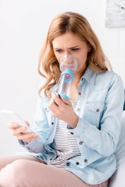 Astımlı bir kadının sprey ve akıllı telefonuyla astım spreyini tutmasının seçici odağı 