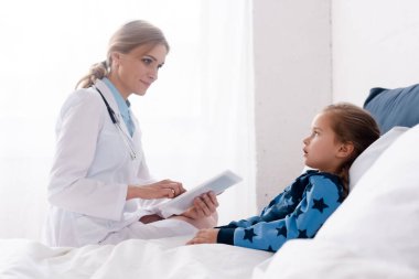 Beyaz önlüklü güzel doktor hasta çocuğun yanında dijital tablet kullanıyor. 