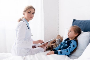 Beyaz önlüklü çekici doktor hasta çocuğun yanında dijital tablet kullanıyor. 