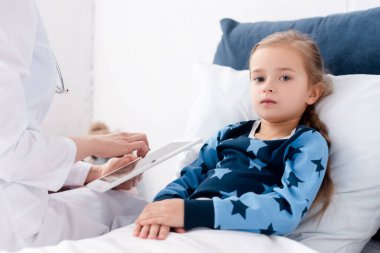 Beyaz önlüklü doktor hasta çocuğun yanında dijital tablet tutuyor. 