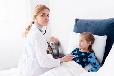 Güzel doktor hasta çocuğu yatak odasında muayene ediyor. 