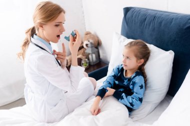 Ağzı açık çekici bir doktor astımlı çocuğun yanında astım spreyi tutuyor. 
