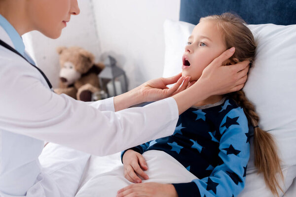 doctor in white coat examining sick child with opened mouth