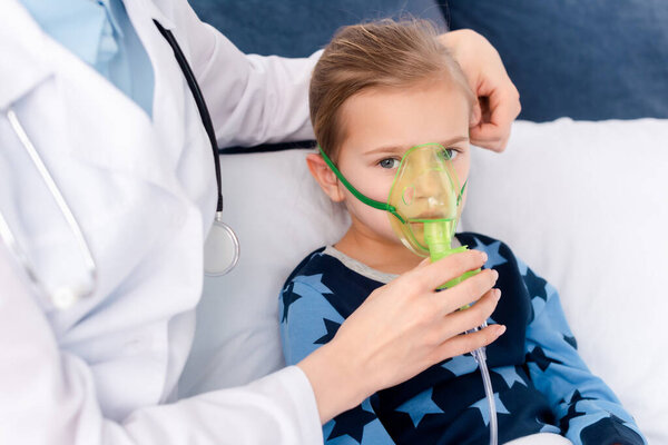 doctor in white coat touching respiratory mask on asthmatic child 