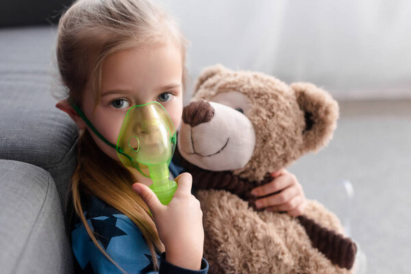 asthmatic kid using respiratory mask and holding teddy bear 
