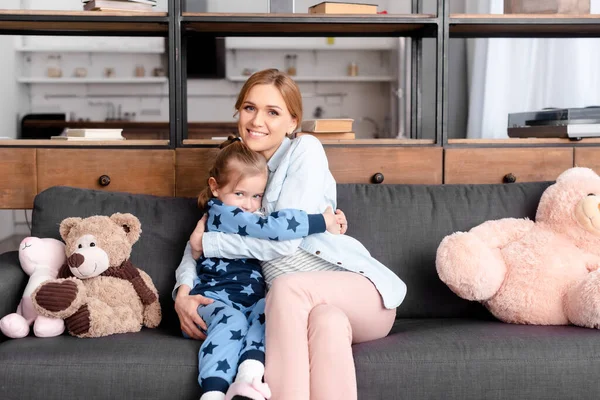 Garoto Bonito Abraçando Mãe Perto Brinquedos Macios Sofá — Fotografia de Stock